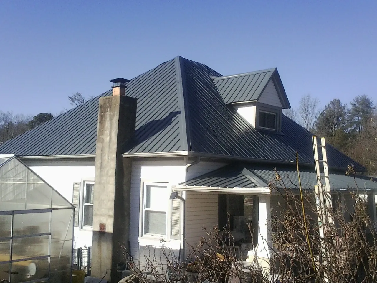 Dark blue standing seam metal roof on a white farmhouse with dormer — Slate & Tile Roof Repair by Roofing Brothers in Mancelona