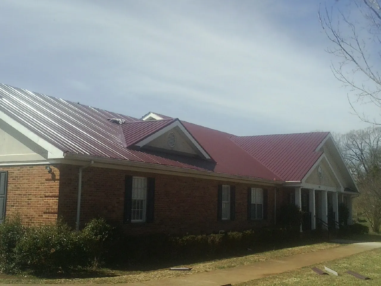 Red metal roof with gabled entries on a long brick building, from a Hail Damage Roof Repair job in Mancelona