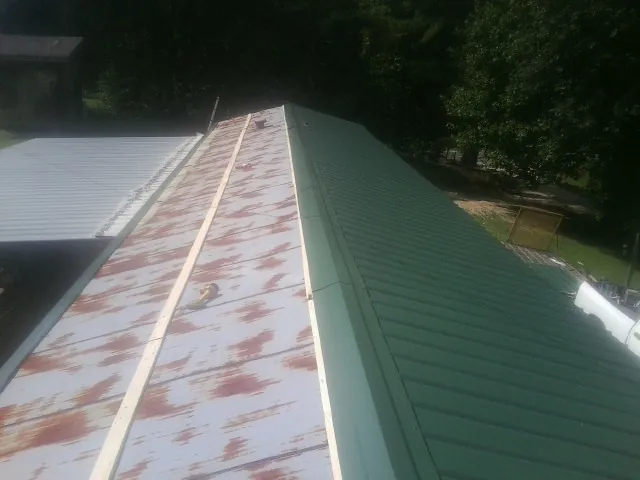 Old rusted panels beside newly installed green metal roofing — Wind Damage Roof Repair by Roofing Brothers in Mancelona