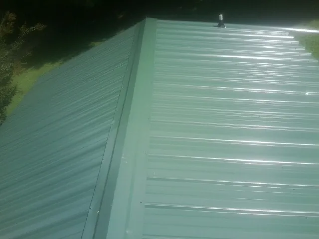 New green metal panels meeting at the ridge of a roof — Flat Roof Repair work by our crew in Mancelona