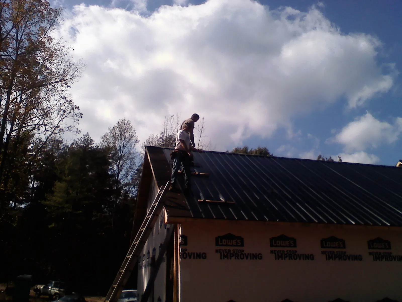 Roofer fastening dark metal panels high against a cloudy sky, from a Roof Inspection job in Mancelona