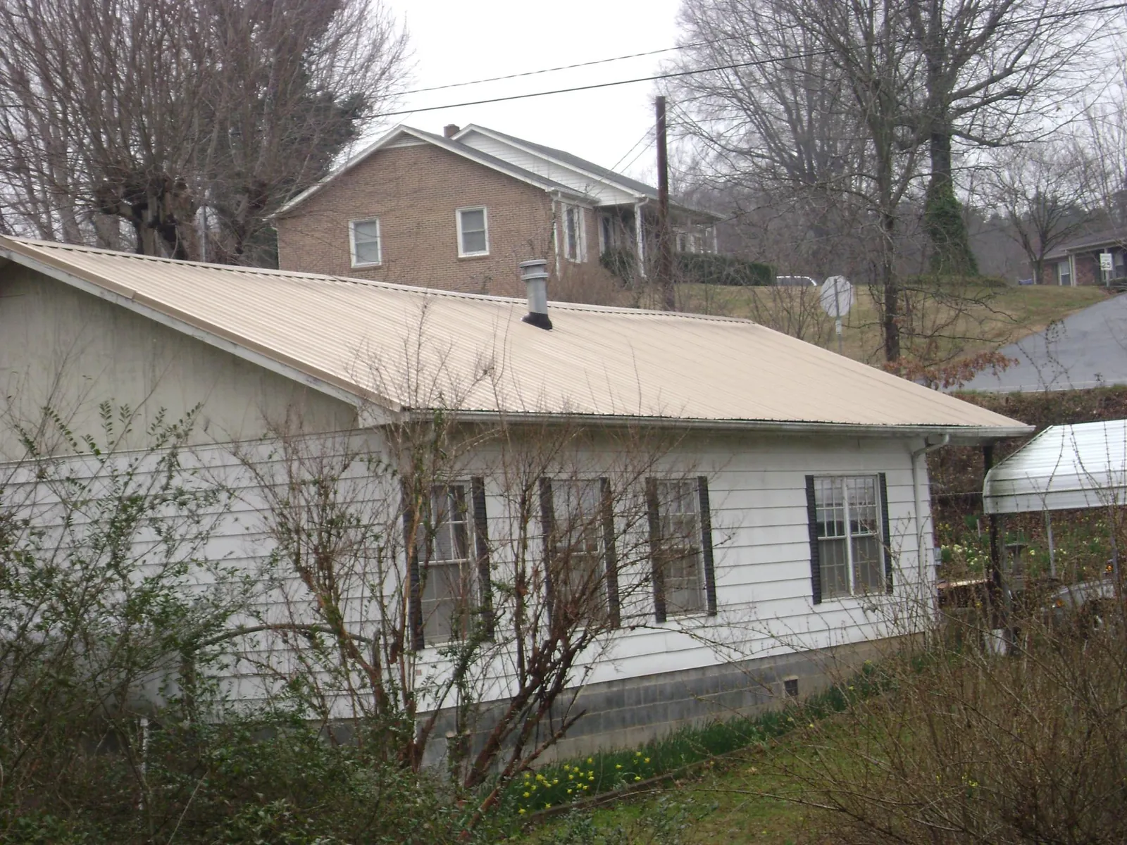 Tan metal roof on a white sided house set into a hillside — Commercial Roofing by Roofing Brothers in Mancelona
