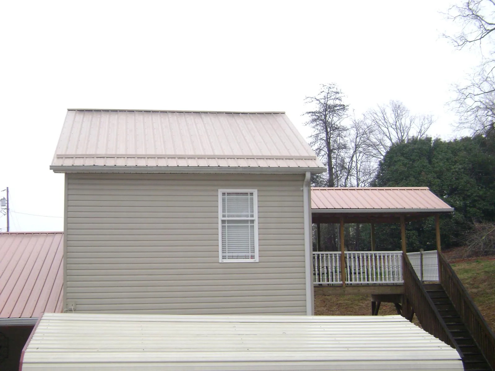Tan metal roofs on a two story addition and attached porch, from a Roof Replacement job in Mancelona