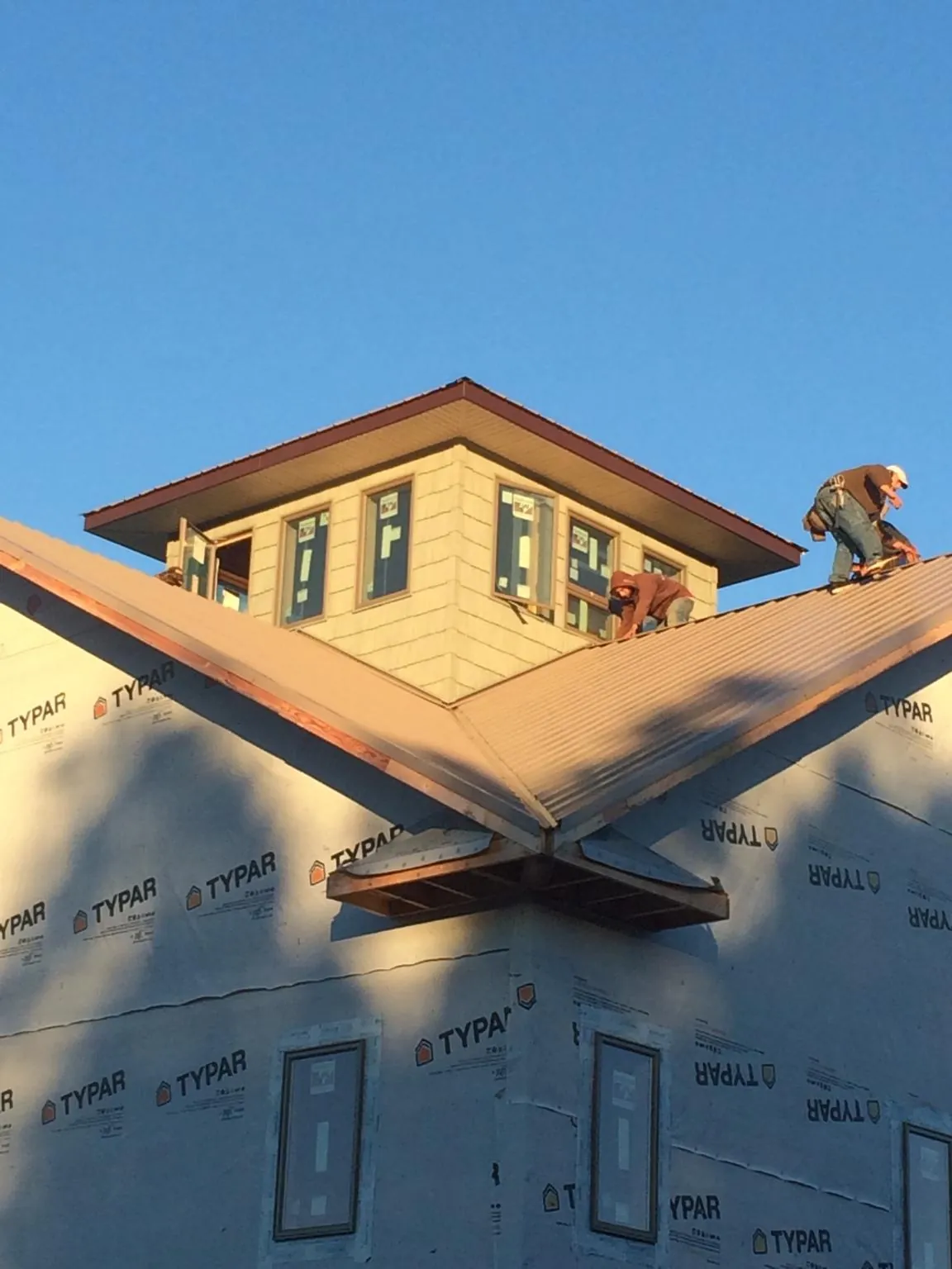 Roofers working around a rooftop cupola on a new metal roof at sunset — Roof Waterproofing in Mancelona by Roofing Brothers